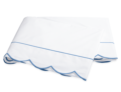 A folded white bedsheet from the Matouk Butterfield Bedding Collection, Ocean, featuring blue scallop detail and a thin blue line, shown on a plain background.