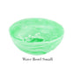 The image shows a small, round, light green bowl with a marbled wave pattern from the Mint Resin Serveware Collection by Nashi Home. Made from shatter-resistant resinware, it’s ideal for stylish home decor. Text reads "Wave Bowl Small.