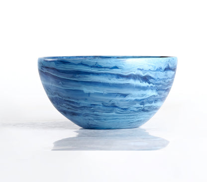 A round ceramic bowl with blue and white marbled patterns, displayed on a reflective white surface—perfect as shatter-resistant decor or paired with the Denim Resin Serveware Collection from Nashi Home for a stylish touch.