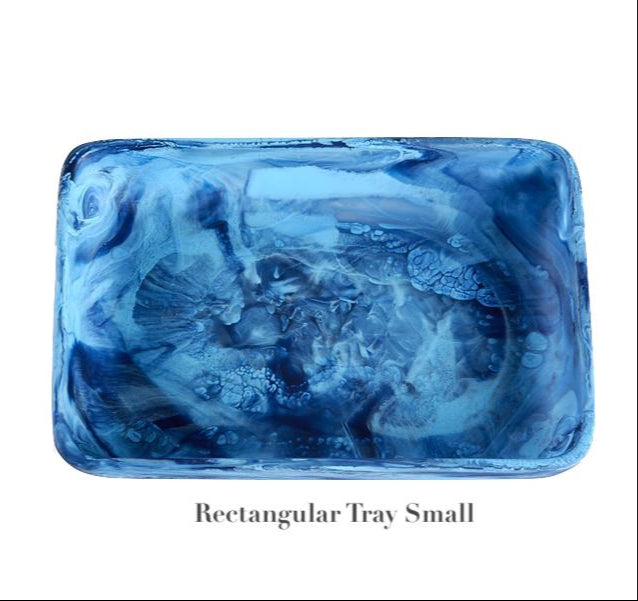 A small, rectangular tray from Nashi Home's Denim Resin Serveware Collection is shown with a blue marbled pattern on a white background. Made from shatter-resistant resinware, it's perfect for stylish home decor. Text below: "Rectangular Tray Small.