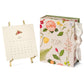The 2026 Classic Desk Calendar Collection by Karen Adams features floral designs and a ribbon, shown with an August 2025 page on a gold stand—an ideal gift or best-selling addition to any calendar selection.