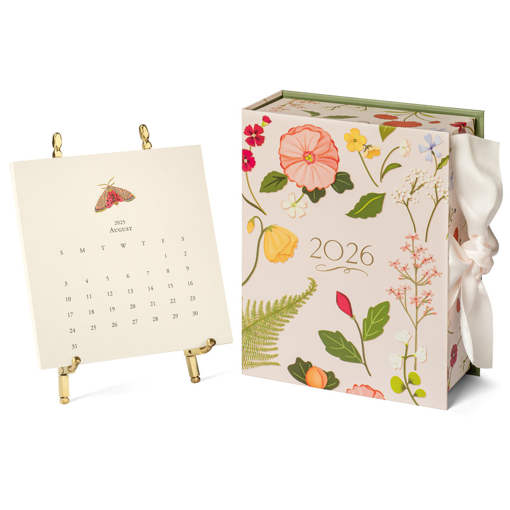 The 2026 Classic Desk Calendar Collection by Karen Adams features floral designs and a ribbon, shown with an August 2025 page on a gold stand—an ideal gift or best-selling addition to any calendar selection.
