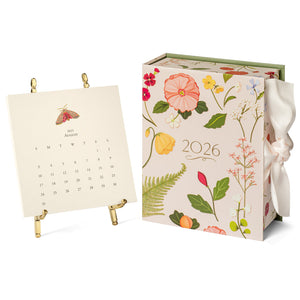 The 2026 Classic Desk Calendar Collection by Karen Adams features floral designs and a ribbon, shown with an August 2025 page on a gold stand—an ideal gift or best-selling addition to any calendar selection.