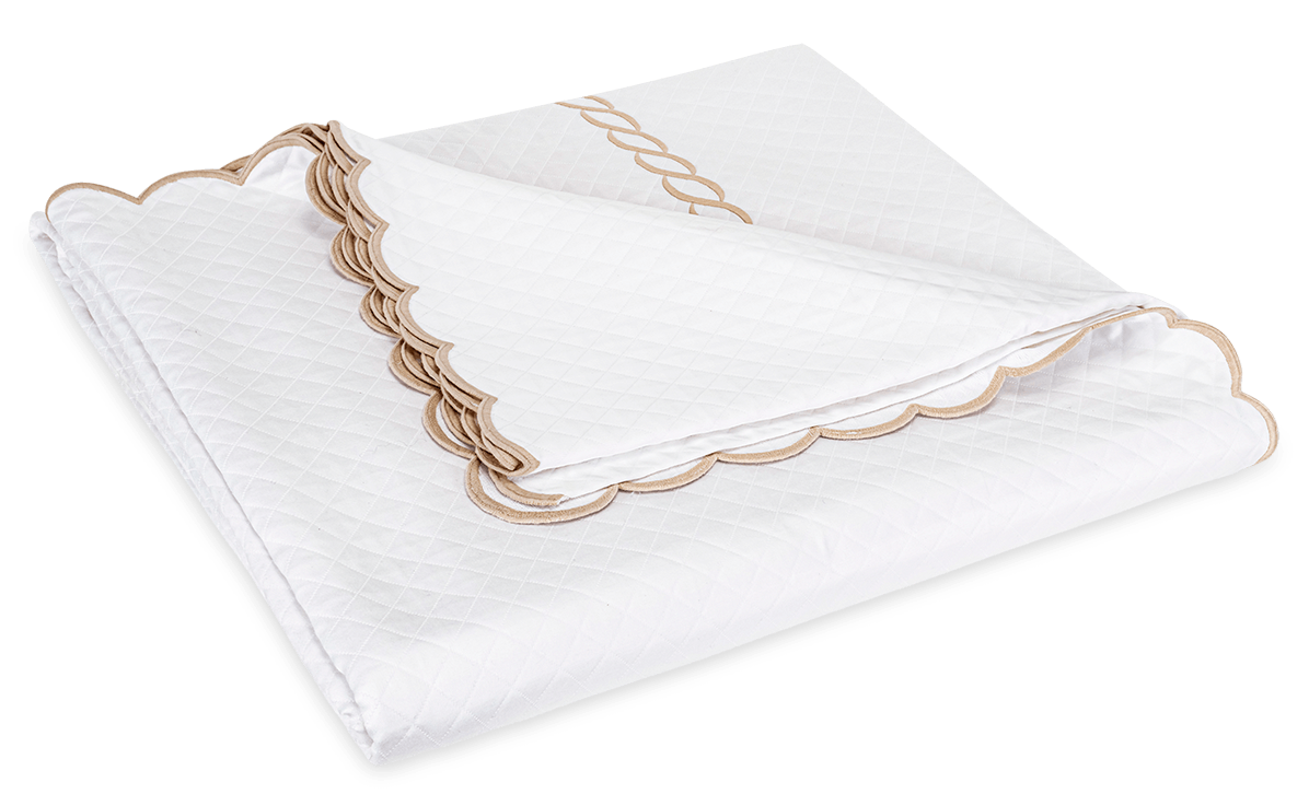 A folded white Matouk Classic Chain Scallop Matelassé blanket from the Dune collection, featuring scalloped beige trim and elegant embroidery along the edge.