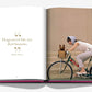 In "Chic Dogs" by Assouline, an open book showcases a quote about the timeless bond between dogs and humans. Alongside, a stylish image captures a person in a headscarf biking with chic flair while their small dog enjoys luxury in the basket.