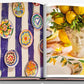 The Assouline book "Marbella Sol" features colorful ceramic plates evoking Marbella's charm on the left page, while a decorative lemon centerpiece alongside a classical bust brings to life a European Miami vibe on the right.
