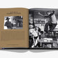 An open book titled "Columbia Pictures" by Assouline features a page of text on the left and a black-and-white photograph of a jumping man in a kitchen scene on the right, capturing a moment from 100 Years of Cinema.