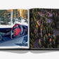 Assouline’s “Cortina d'Ampezzo” book open: left page features a driver grasping a red Ferrari wheel; right page shows an aerial of a winding forest road in the Dolomites.