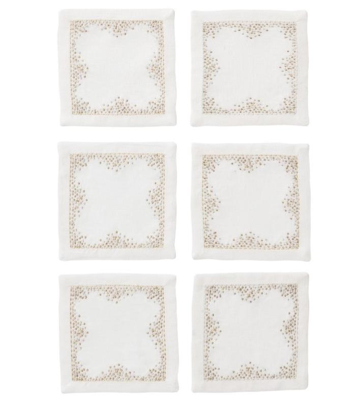 The Kim Seybert Pin Dot Cocktail Napkin Set features six white linen napkins with beige embroidered borders, arranged in two rows of three on a white background—perfect for adding elegance to your table setting.