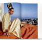 Draped in Vendome's Caftans: From Classical to Camp and a lavish headpiece, a person sits elegantly on an orange blanket against the breathtaking mountainous backdrop—a perfect resort setting for this display of style.