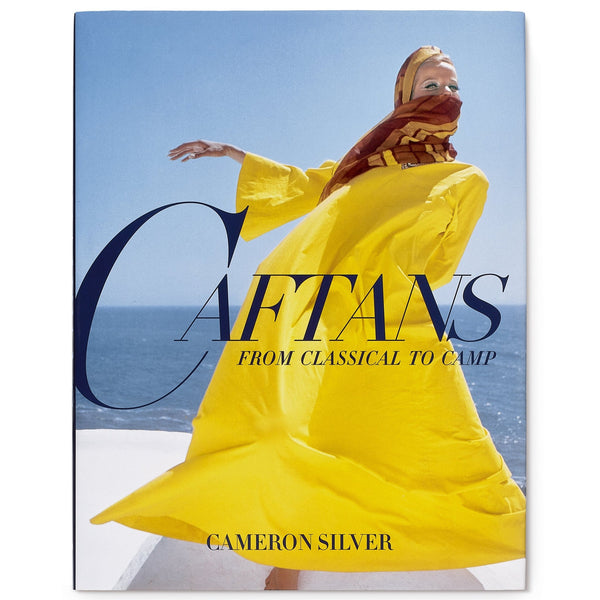 The book cover features a woman in a yellow caftan and headscarf against a blue sky and ocean. Titled "Caftans: From Classical to Camp" by Vendome, it embodies the essence of Caftan Couture with an air of resort elegance.