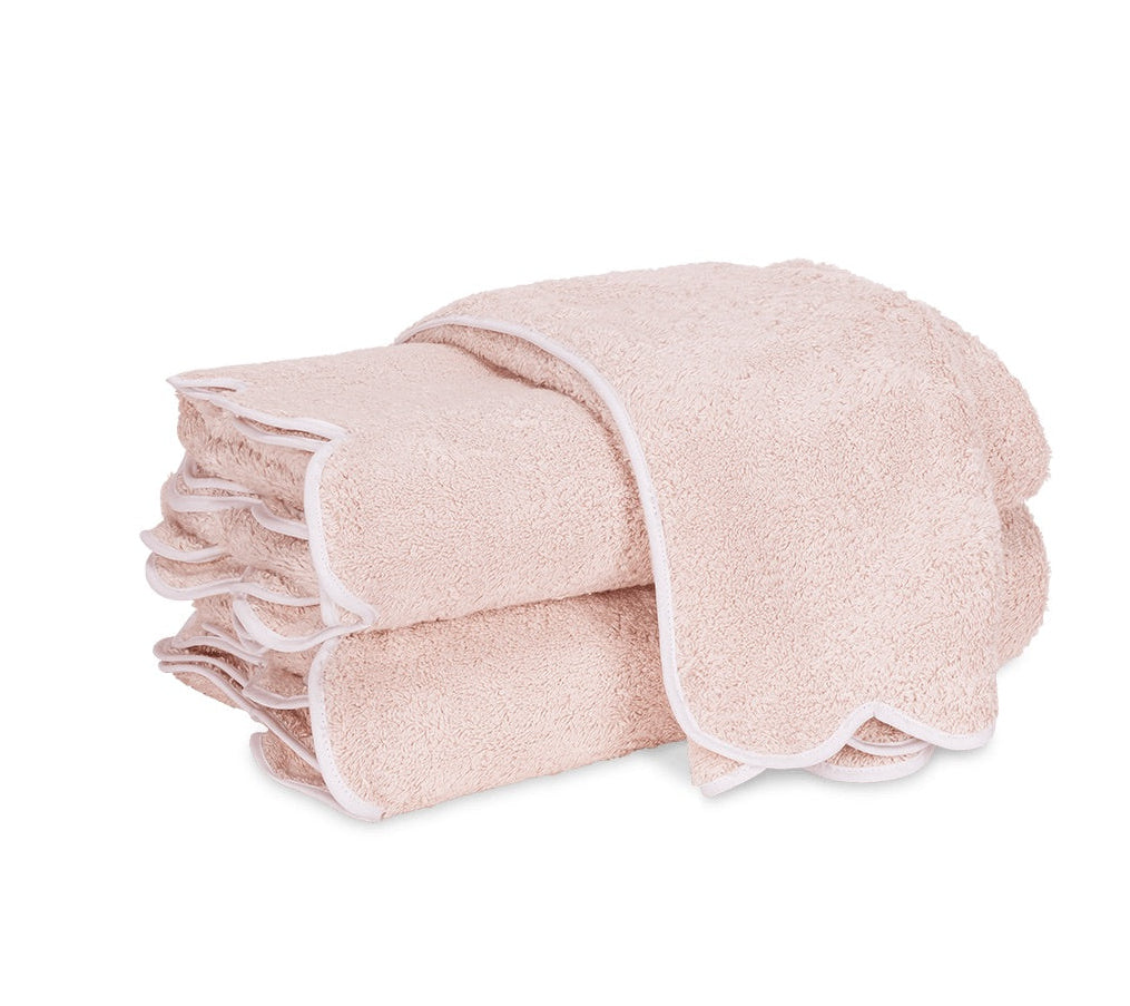 Two folded light pink luxury bath towels from the Matouk Cairo Scallop Bath Collection, featuring elegant white scalloped trim and expertly crafted in the USA from long-staple cotton, stacked on a white background.
