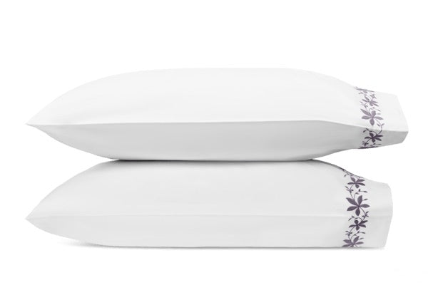 Two white pillows from the Matouk Callista Bedding Collection are stacked atop one another, each crafted from luxurious Giza Egyptian cotton and featuring an elegant purple floral pattern along the right edge.