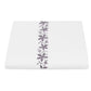 A folded white napkin from the Callista Bedding Collection by Matouk features a vertical strip of decorative embroidery with purple floral accents in the center, displayed on a plain white background.