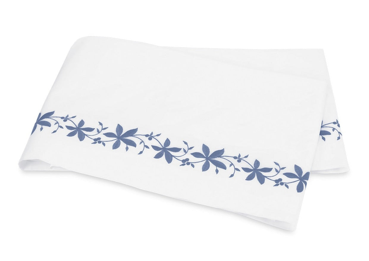 A folded white sheet from the Callista Bedding Collection by Matouk, featuring a blue floral pattern along the edge, crafted from luxurious Giza Egyptian cotton with a 500 thread count, and displayed on a plain background.