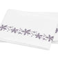 A folded white bed sheet from the Matouk Callista Bedding Collection, expertly crafted from luxurious Giza Egyptian cotton with a 500 thread count, showcasing a delicate purple floral pattern and decorative embroidery along one edge, displayed on a plain background.