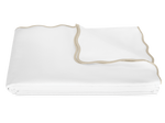 The Camilla Pique Coverlet by Matouk is a neatly folded white blanket with beige trim and a delicate scallop edge, displayed on a plain white background.