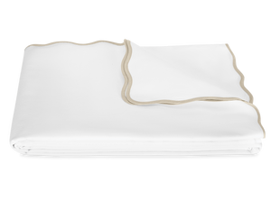 The Camilla Pique Coverlet by Matouk is a neatly folded white blanket with beige trim and a delicate scallop edge, displayed on a plain white background.