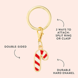 The Foggy Dog Candy Cane Collar Charm is a gold keychain featuring a double-sided red and white candy cane, with a split ring and clasp attachment. Made of durable hard enamel, this festive accessory is perfect for collars.