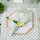 A place setting with a hexagonal plate, Kim Seybert Provence Napkin Set, parrot-shaped napkin ring, beaded placemat, bamboo-handled flatware, matching tablecloth, and a green plant nearby.