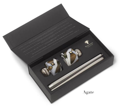 An open black box showcases two intricately designed hand-blown glass bottle stoppers, accompanied by a metal rod labeled "Agate," reflecting the elegance of the Baobab Collection Candle Holder Twins by Baobab.