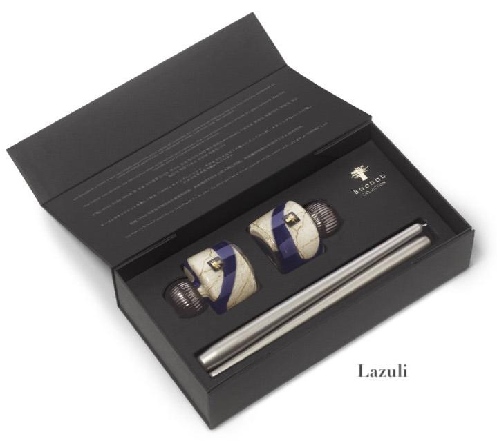A black box features the Baobab Collection Candle Holder Twins, showcasing a pair of ceramic stoppers with a blue and white design and an elegant metal wine pourer. The lid is adorned with the brand's logo and text. Ideal for decorative object enthusiasts, this set enhances any collection or occasion with its charm.