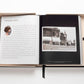 A large open book lies on a white surface, displaying text and a black-and-white photo of a Chanel storefront on the right page. The Impossible Collection of Chanel by Assouline, capturing Gabrielle Chanel's legacy, is nestled in a beige box with a black ribbon bookmark visible, exuding an air of luxe minimalism.