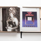 An open book displays a black-and-white photograph of a woman holding a perfume bottle on the left page and a color advertisement for The Impossible Collection of Chanel by Assouline on the right, embodying luxe minimalism and timeless elegance in every detail.