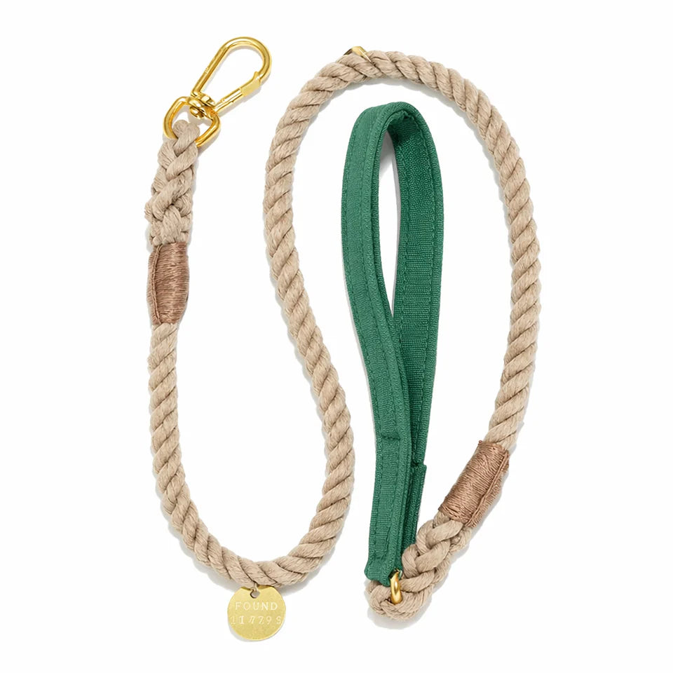 The Waxed Cotton Canvas Leash Collection by Found My Animal features a beige rope leash with gold hardware, green fabric handle, and a round “FOUND 1799” tag. Handcrafted for style and durability on daily walks.