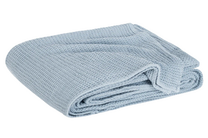 The Matouk Chatham Blanket in Hazy Blue, crafted in Portugal from 100% cotton with a waffle texture, is shown folded against a white background.