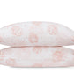 Two white pillows from the Tillett Chrysanthemum Bedding Collection by Matouk, featuring a pale pink Chrysanthemum-inspired floral motif, are stacked against a white background to highlight the collection’s elegant design.