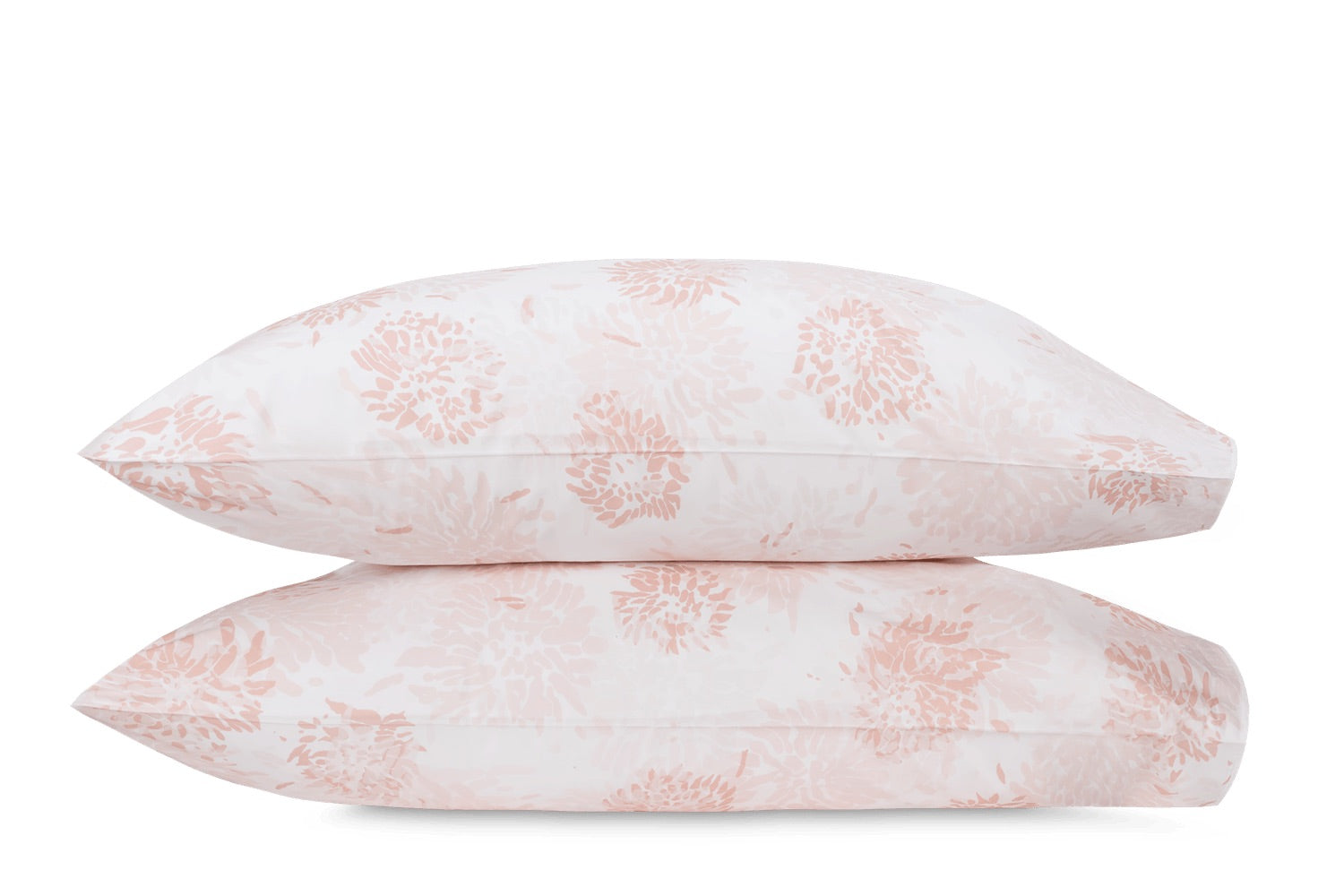 Two white pillows from the Tillett Chrysanthemum Bedding Collection by Matouk, featuring a pale pink Chrysanthemum-inspired floral motif, are stacked against a white background to highlight the collection’s elegant design.
