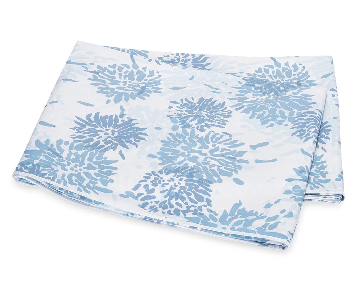 The Tillett x Matouk Chrysanthemum Bedding Collection in blue by Matouk showcases folded white fabric with a blue chrysanthemum floral motif, displayed on a plain background.