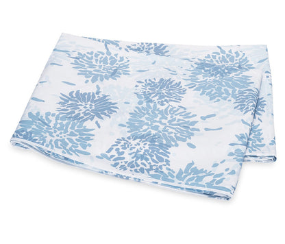 The Tillett x Matouk Chrysanthemum Bedding Collection in blue by Matouk showcases folded white fabric with a blue chrysanthemum floral motif, displayed on a plain background.