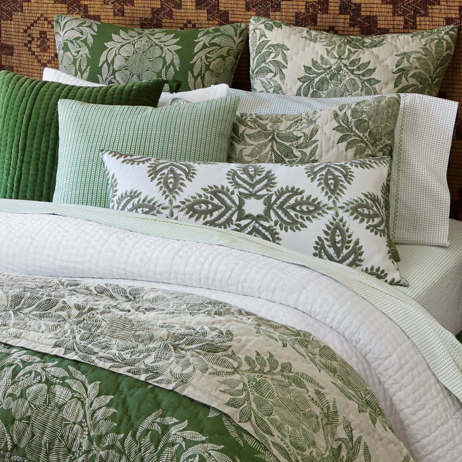 A neatly made bed featuring green and white pillows, a quilted green throw pillow, the John Robshaw Cinde Sage Bedding Collection comforter set, and a soft organic sheet set for an inviting touch.