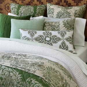 A neatly made bed featuring green and white pillows, a quilted green throw pillow, the John Robshaw Cinde Sage Bedding Collection comforter set, and a soft organic sheet set for an inviting touch.
