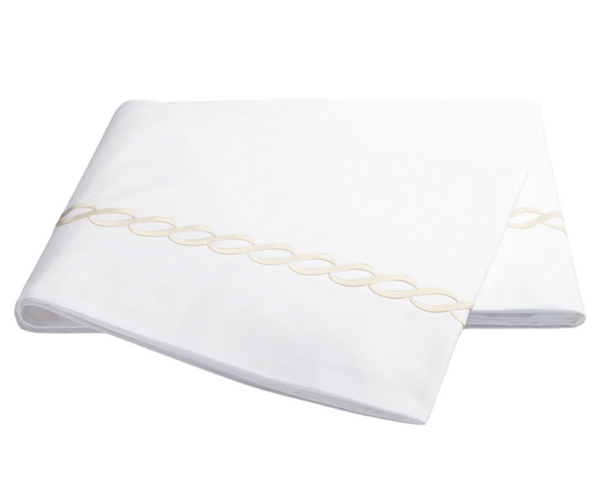 The Matouk Classic Chain Bedding Collection, Ivory, features a white folded sheet with a beige Greek motif braided pattern near the edge. Crafted from cotton percale, this elegant piece is OEKO-TEX certified for high safety and environmental standards.