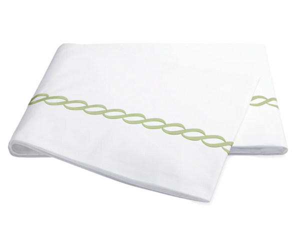 White bedsheet from the Matouk Classic Chain Bedding Collection with a green intertwined chain pattern resembling a Greek motif, crafted from luxurious cotton percale.