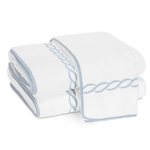Two folded white cotton terry towels from the Matouk Classic Chain Bath Collection, featuring light blue embroidered borders and a twisted rope design, are stacked on a plain white background.