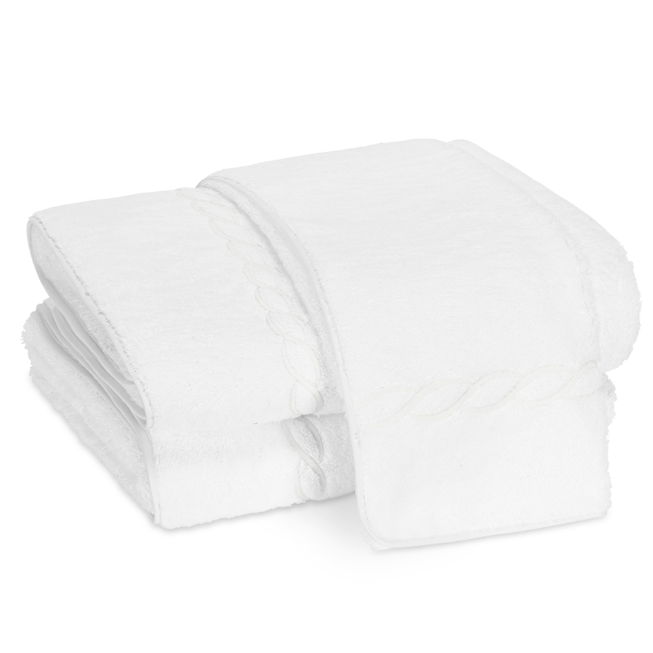 A stack of white bath towels from the Matouk Classic Chain Bath Collection, featuring a subtle decorative border and crafted from Cairo cotton terry, neatly folded on a plain white background.