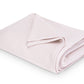 The Costa Mesa Blanket Collection by Matouk features a soft, light pink knitted blanket displayed on a white background.