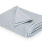 The Costa Mesa Blanket Collection by Matouk is displayed, featuring a neatly folded light grey blanket with a soft knitted texture on a white background.