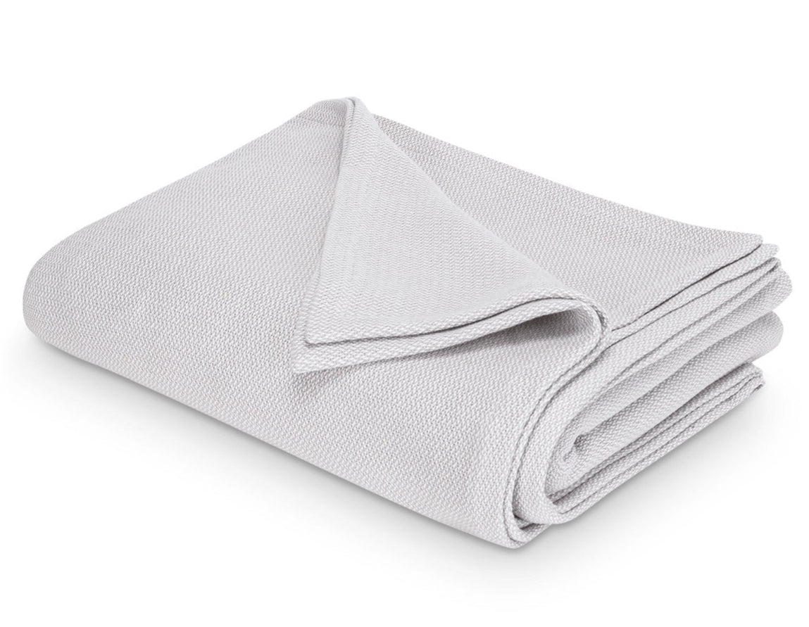The Costa Mesa Blanket Collection by Matouk features a neatly folded light gray blanket with a soft knitted texture, shown on a white background.