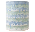 The Cylindrical Garden Stool Collection by Paul Schneider Ceramics features ceramic stools with blue and green drip glaze over white. Each piece is unique, making it a perfect addition to any decor.