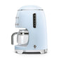 The light blue SMEG Drip Filter Coffee Machine Collection by Smeg includes a glass carafe, silver accents, side control buttons, and an eco-friendly reusable coffee filter.