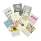 The Dogwood-Hill 2026 Desktop Calendar Set features illustrated cards with original artwork for each month, arranged in a circle around a yellow floral envelope.