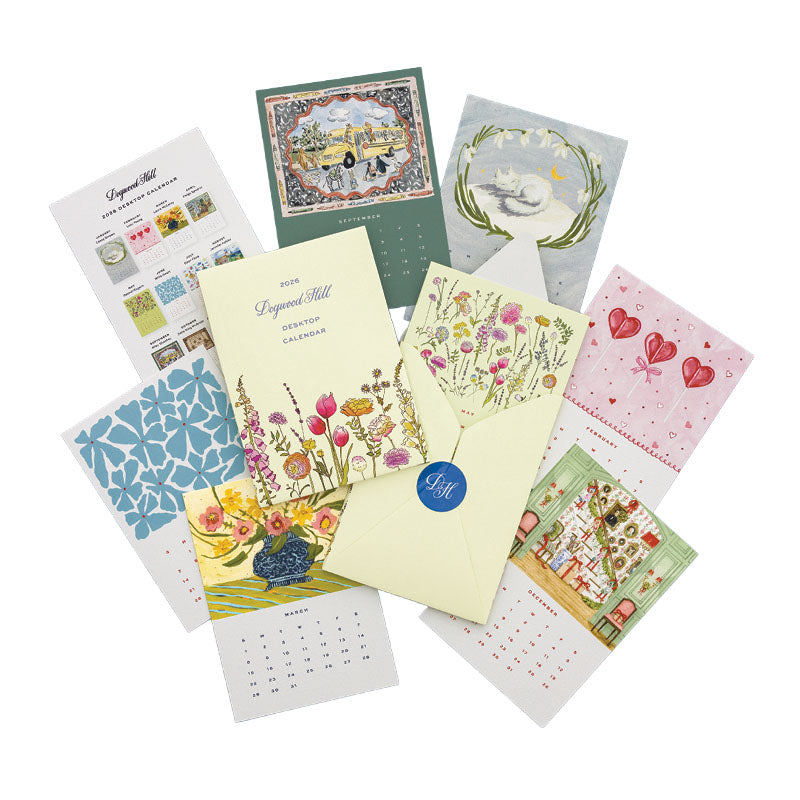 The Dogwood-Hill 2026 Desktop Calendar Set features illustrated cards with original artwork for each month, arranged in a circle around a yellow floral envelope.