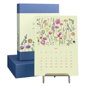 The Dogwood-Hill 2026 Desktop Calendar Set features a floral-themed May page on a stand with original artwork, and a closed gift box and lid in the background.
