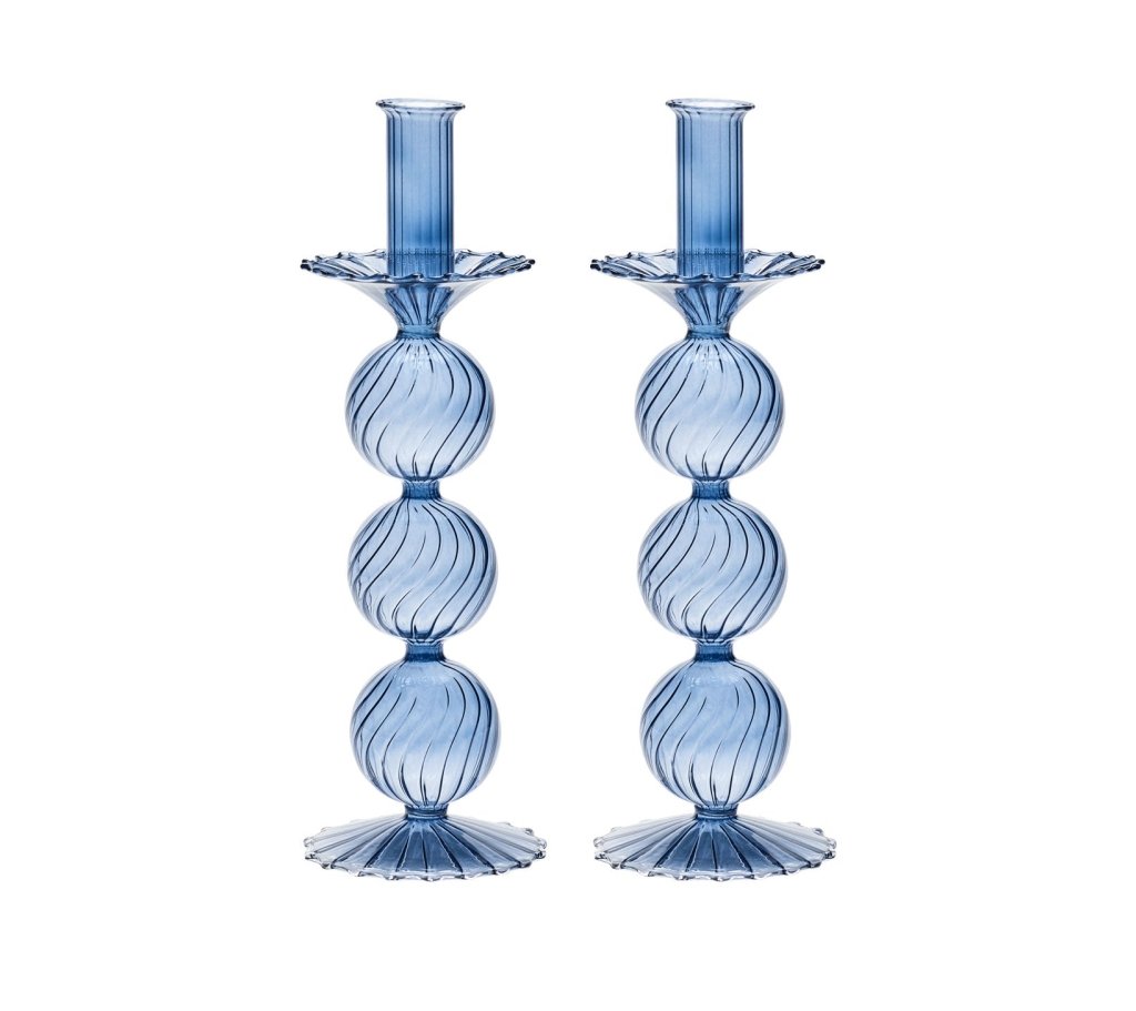 The Iris Tall Candle Holder Set by Kim Seybert features two identical blue, hand-blown glass holders with ribbed, spherical, and fluted designs and elegant scalloped bases, displayed side by side on a white background.