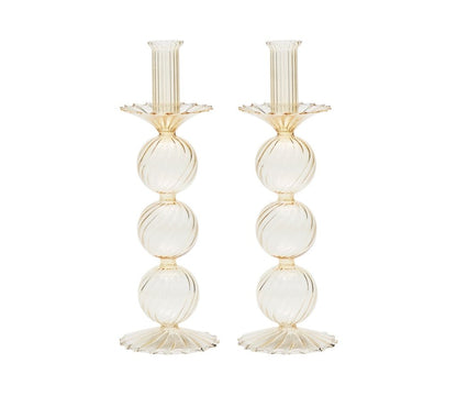 The Kim Seybert Iris Tall Candle Holder Set features two hand-blown glass candlesticks with a ribbed texture, three stacked spheres, and scalloped bases, shown against a white background.